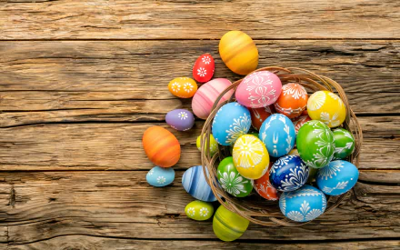 Colorful decorated Easter eggs in a woven basket on rustic wooden planks — holiday Easter scene, 2K Quad HD PC desktop wallpaper background.