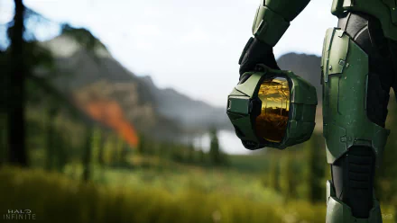 HD wallpaper featuring Master Chief from Halo Infinite, standing against a lush, mountainous background, holding his helmet by his side.