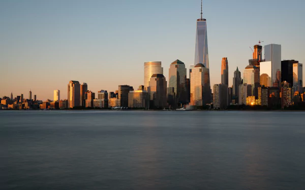 Sunset view of Manhattan skyscrapers, including the One World Trade Center, with the calm river in the foreground, captured in 8K Ultra HD resolution.