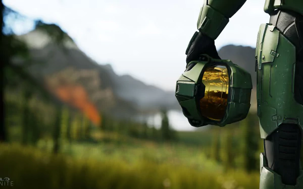 HD wallpaper featuring Master Chief from Halo Infinite, standing against a lush, mountainous background, holding his helmet by his side.