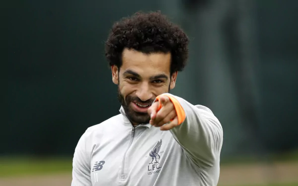 Egyptian soccer player smiling and pointing at the viewer in a training top — sports-themed 2K Quad HD PC desktop wallpaper background.