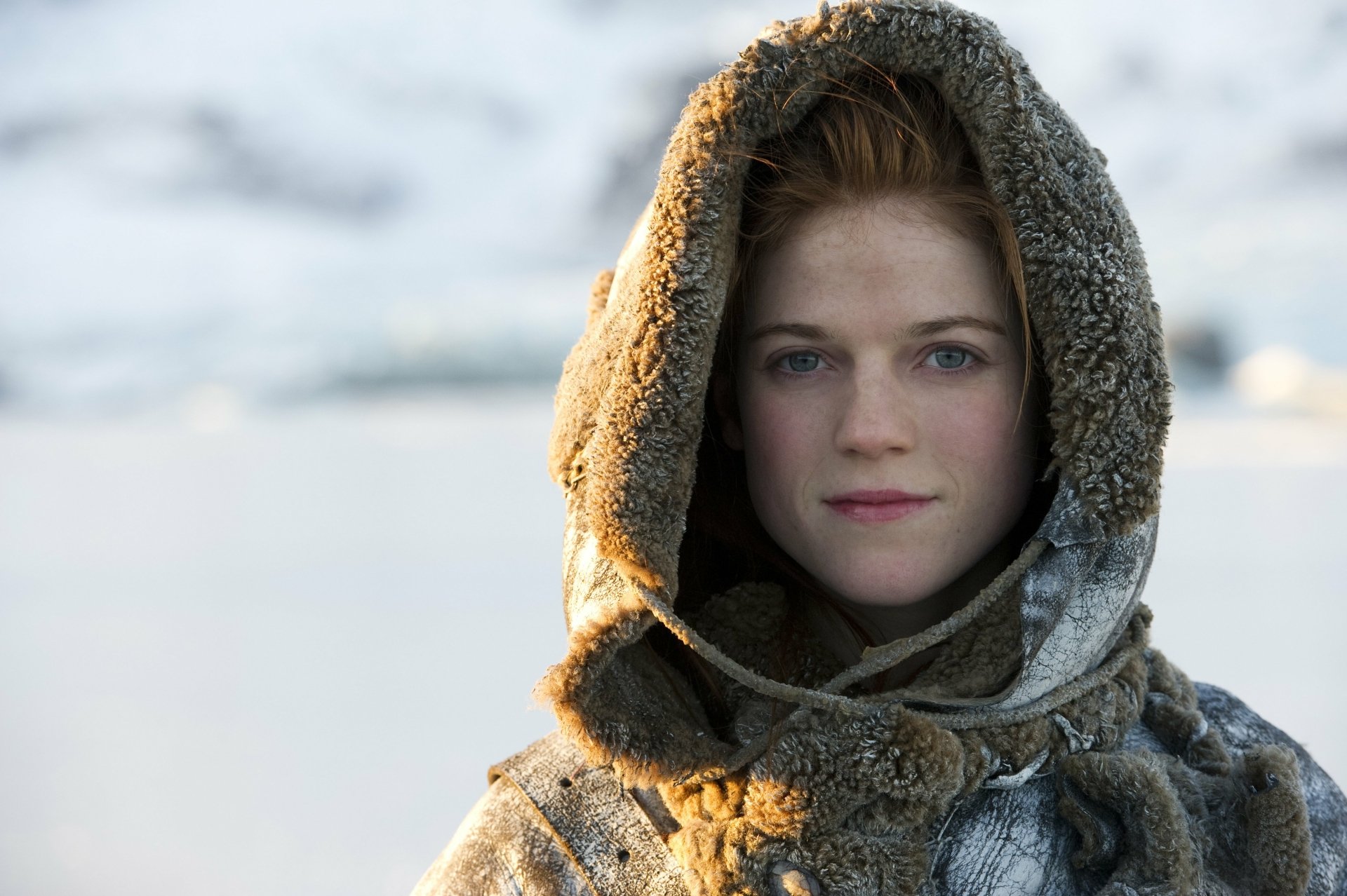 Rose Leslie as Ygritte in Game of Thrones, wearing a fur-lined hood in a snowy landscape, with her blue eyes gazing ahead. HD desktop wallpaper.