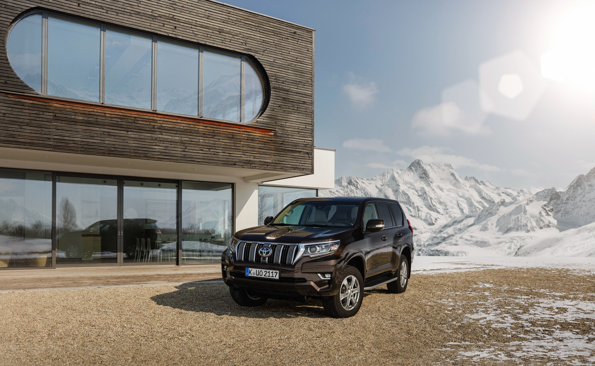 Black Toyota Land Cruiser SUV car parked outside a modern house with snow-capped mountains under bright sun — 4K Ultra HD PC desktop wallpaper