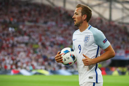 HD wallpaper of English soccer player Harry Kane in his national team jersey, holding a ball on the field during a match.