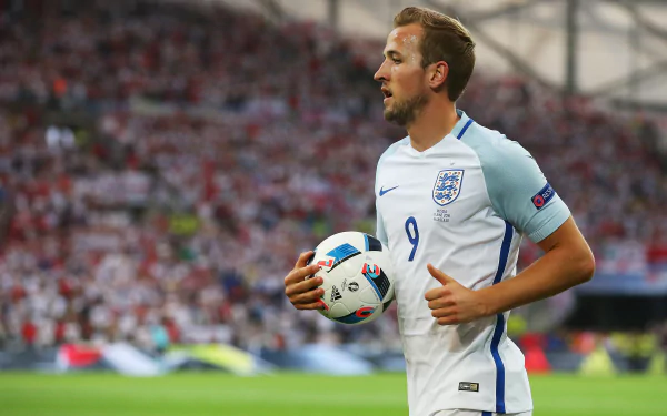 HD wallpaper of English soccer player Harry Kane in his national team jersey, holding a ball on the field during a match.