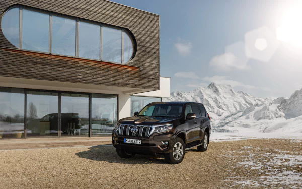 Black Toyota Land Cruiser SUV car parked outside a modern house with snow-capped mountains under bright sun — 4K Ultra HD PC desktop wallpaper