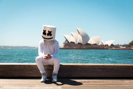 Marshmello, the DJ, sits near the Sydney Opera House on a sunny day. This HD wallpaper captures the blend of modern music artistry with an iconic Australian landmark.