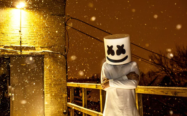Marshmello, the DJ, stands outside under a softly lit snowy night, arms crossed. This HD desktop wallpaper captures the iconic music artist in a serene winter scene.