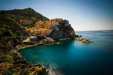HD desktop wallpaper of Manarola, a vibrant village perched on cliffs along the coast of the Cinque Terre in Italy, with a tranquil blue sea and clear horizon.