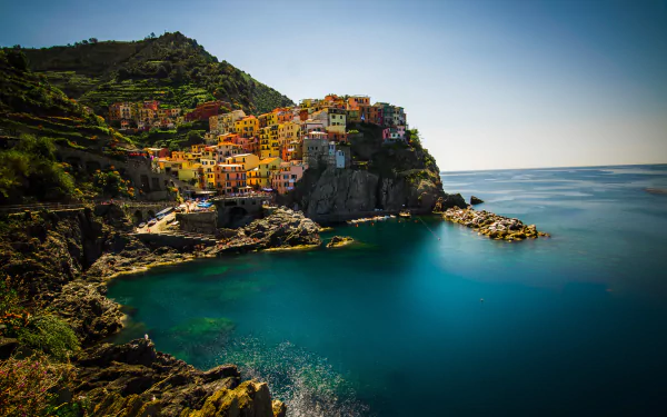 HD desktop wallpaper of Manarola, a vibrant village perched on cliffs along the coast of the Cinque Terre in Italy, with a tranquil blue sea and clear horizon.