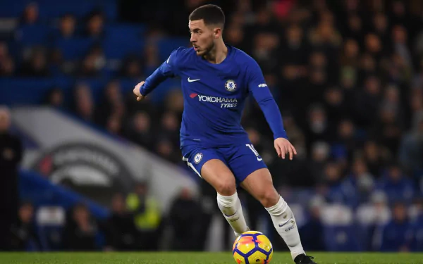HD wallpaper featuring a focused Eden Hazard in a blue Chelsea kit controlling a football on the pitch.