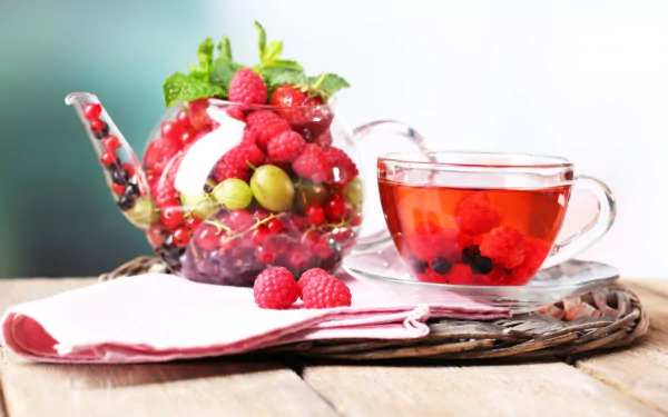 HD PC desktop wallpaper/background: glass teacup of red berry tea beside a teacup-shaped bowl of raspberries and mixed berries — raspberry fruit food on a napkin.