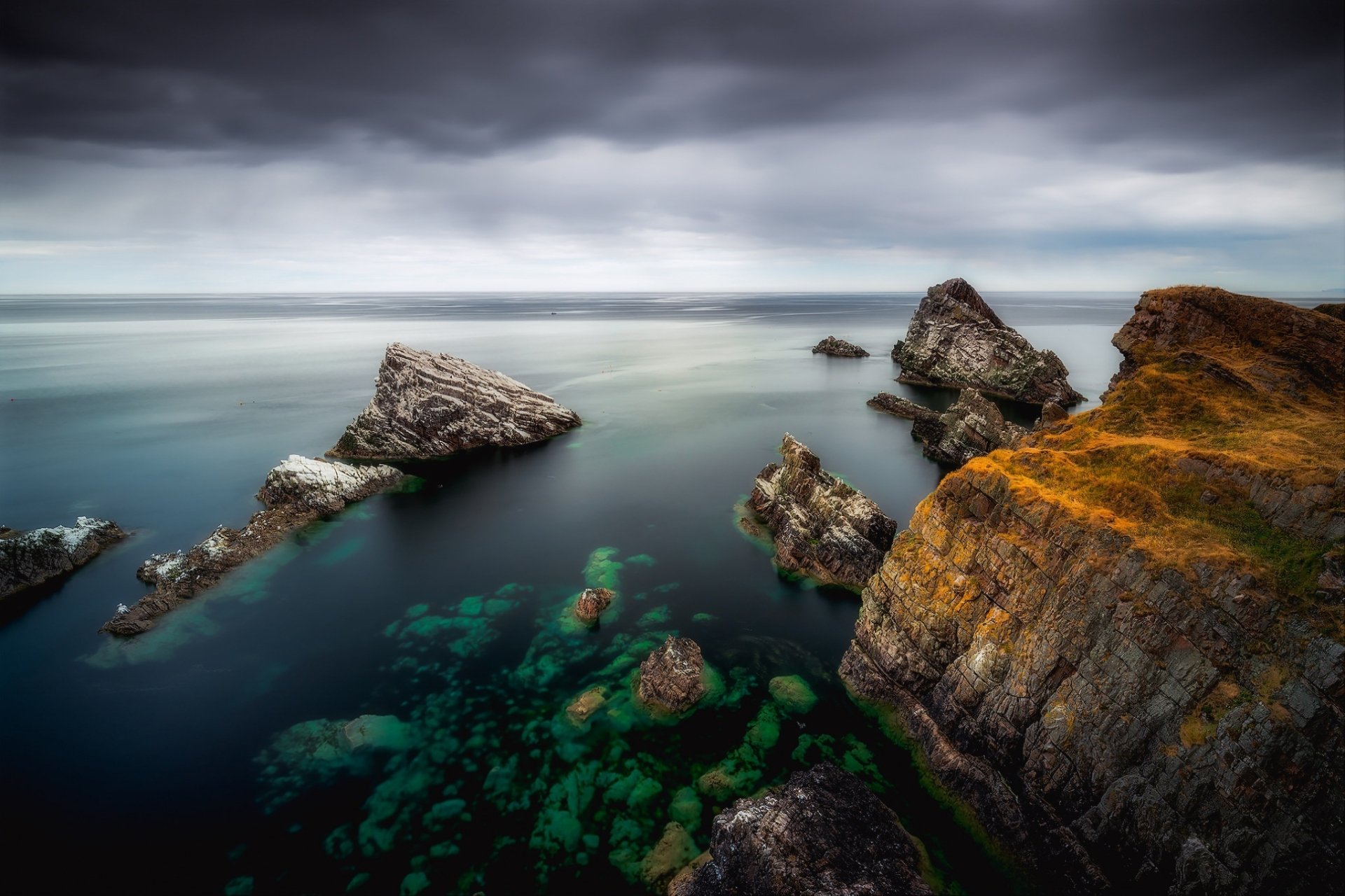 HD PC desktop wallpaper depicting a serene ocean scene with rocky formations and a misty horizon under an overcast sky.
