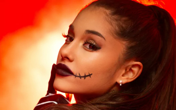 HD desktop wallpaper of a brunette woman with brown eyes, dramatic makeup and stitch-style lipstick, wearing earrings against a glowing orange-red background.
