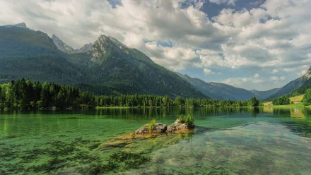 HD desktop wallpaper of a serene lake surrounded by lush forests and towering mountains in Bavaria, Germany, under a partly cloudy sky.