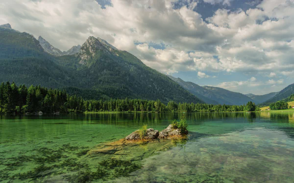 HD desktop wallpaper of a serene lake surrounded by lush forests and towering mountains in Bavaria, Germany, under a partly cloudy sky.