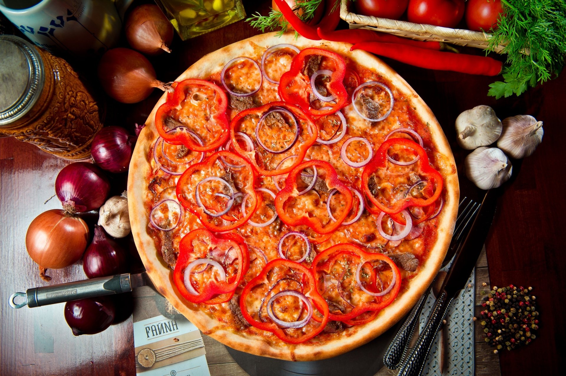 HD still life desktop wallpaper featuring a vibrant pizza topped with red bell peppers and onions, surrounded by garlic, onions, spices, and fresh herbs.