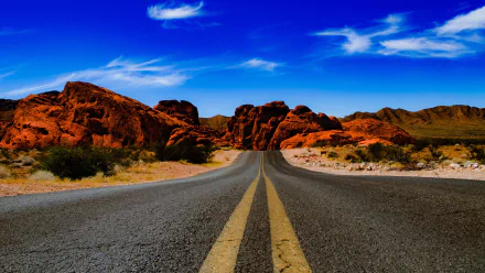 A high-definition wallpaper featuring a man-made road in Nevada, surrounded by vibrant red rock formations under a clear blue sky.