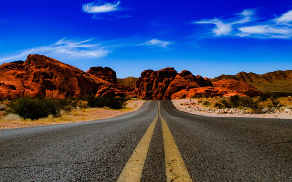 A high-definition wallpaper featuring a man-made road in Nevada, surrounded by vibrant red rock formations under a clear blue sky.