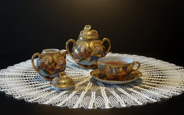 A 4K Ultra HD still life of an ornate teapot, creamer, and teacup filled with tea, all placed on a lace doily against a dark background.