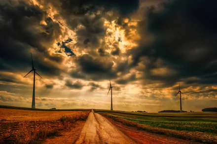 HD PC desktop wallpaper featuring a dirt road leading through fields with tall man-made windmills under dramatic cloud-filled skies.