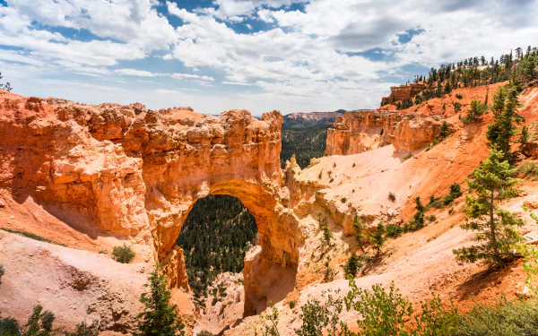Stunning 4K Ultra HD view of a natural sandstone arch and vibrant canyon landscape at Bryce Canyon National Park under a partly cloudy sky.