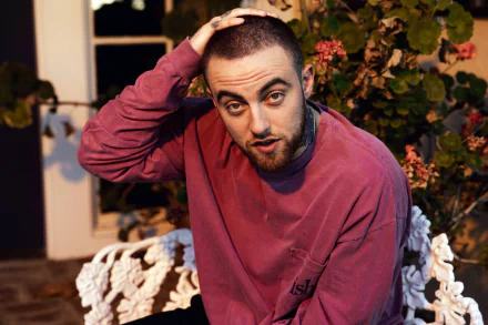 HD desktop wallpaper and background featuring a man in a purple sweatshirt with a contemplative expression, hand on head, sitting by flowers.