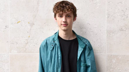HD desktop wallpaper featuring a person standing against a marble backdrop, sporting a teal jacket and black shirt.