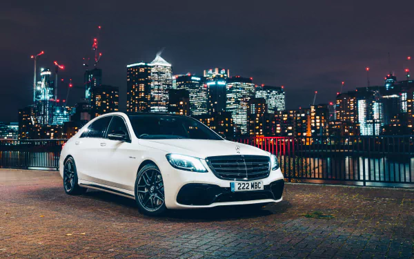 4K Ultra HD PC desktop wallpaper of a white Mercedes-AMG S63 Mercedes-Benz parked on a riverfront promenade with a glowing city skyline at night.