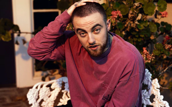 HD desktop wallpaper and background featuring a man in a purple sweatshirt with a contemplative expression, hand on head, sitting by flowers.