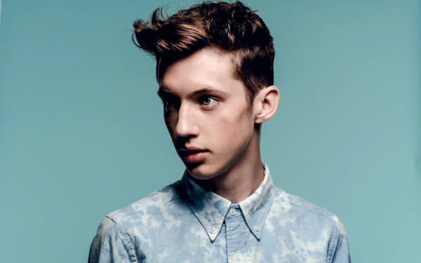 HD desktop wallpaper featuring a portrait of a young man with stylish hair and a blue patterned shirt against a teal background.