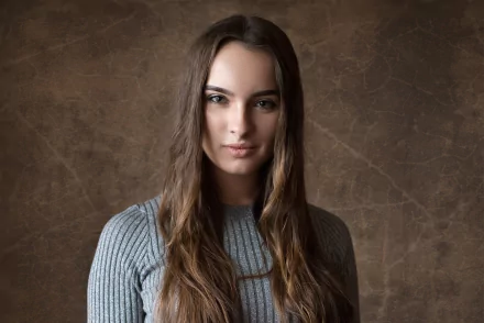 HD desktop wallpaper of a brunette model with long hair and striking green eyes against a textured brown background.