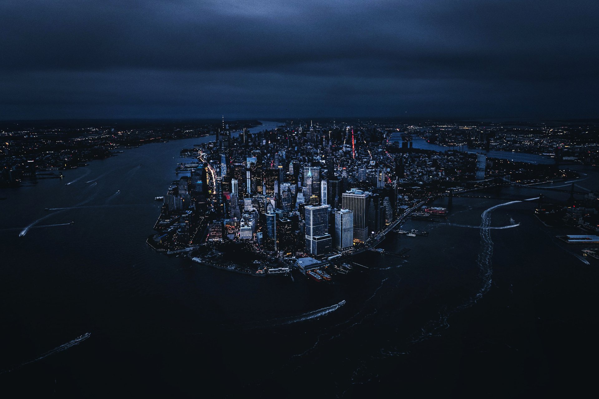 A nighttime aerial view of New York City with illuminated skyscrapers and waterways, captured as a high-definition man-made urban landscape for desktop wallpaper.