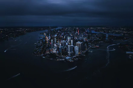 A nighttime aerial view of New York City with illuminated skyscrapers and waterways, captured as a high-definition man-made urban landscape for desktop wallpaper.