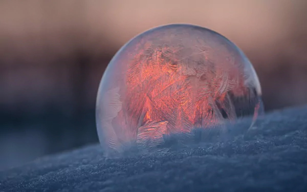 HD desktop wallpaper of a frozen ice bubble resting on snow, glowing softly with warm light against a blurred natural background.