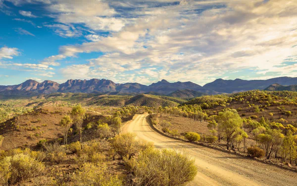 HD desktop wallpaper featuring a winding dirt road through a natural landscape with sparse vegetation under a partly cloudy sky.