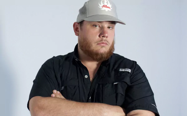 HD desktop wallpaper featuring a posed man in a cap with crossed arms against a neutral background.