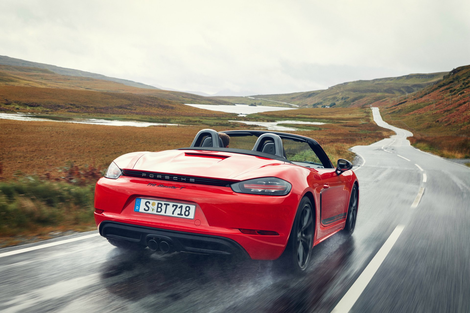 A red Porsche 718 Boxster GTS driving on a winding road through a scenic, open landscape, captured in a 4K Ultra HD desktop wallpaper.