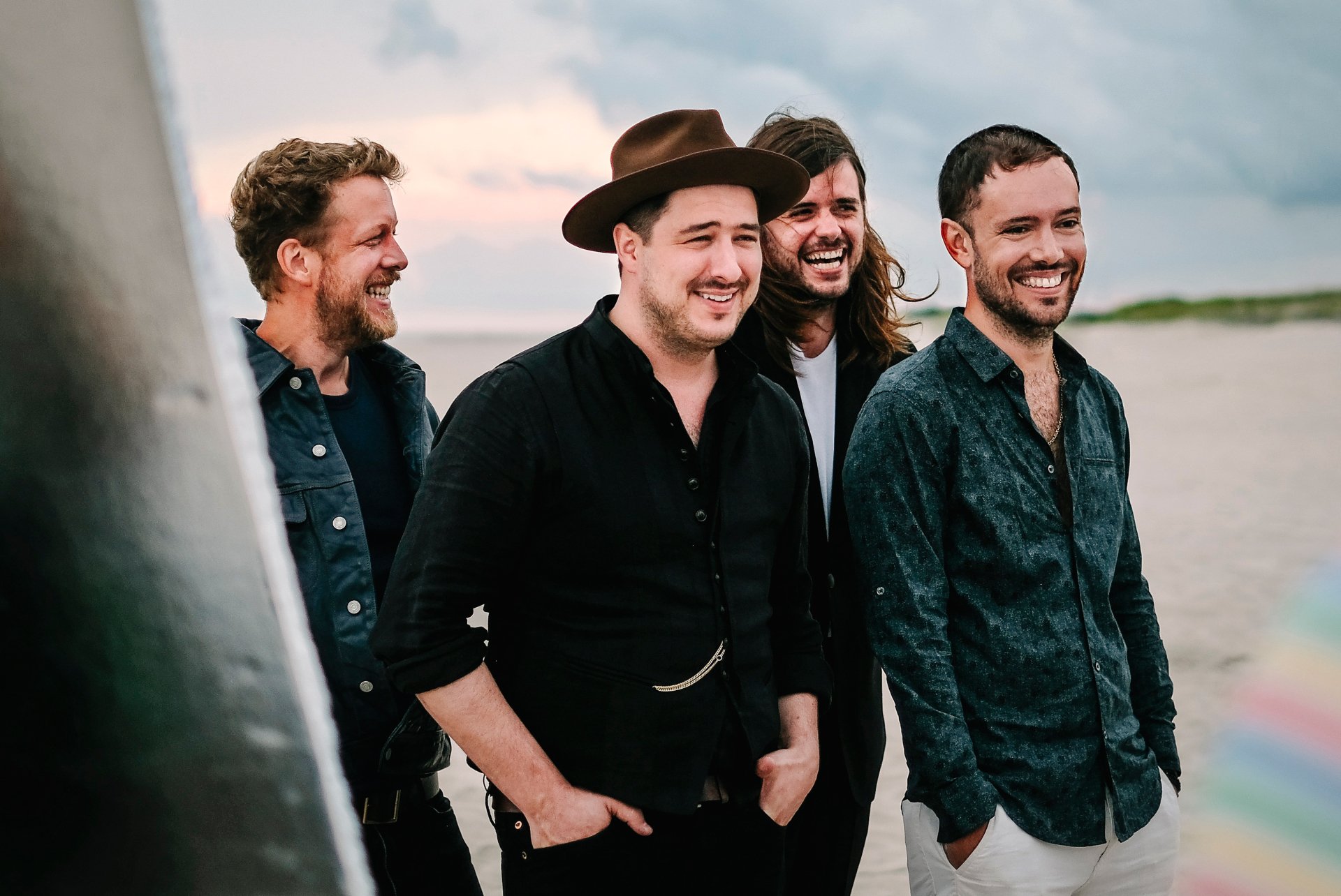HD desktop wallpaper featuring the band Mumford & Sons casually posing with a beach backdrop.