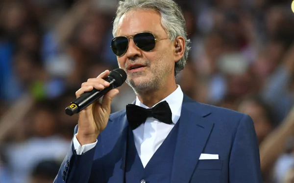 HD wallpaper featuring Andrea Bocelli in a suit with sunglasses, holding a microphone.