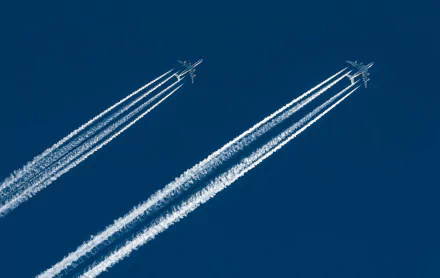 HD desktop wallpaper featuring two passenger planes soaring across a deep blue sky, leaving white contrails in their wake.