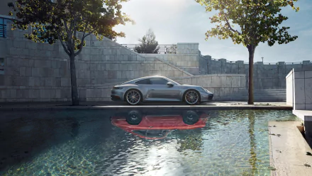 Silver Porsche 911 Carrera parked beside a reflecting pool with modern stone walls and trees — HD PC desktop wallpaper background.