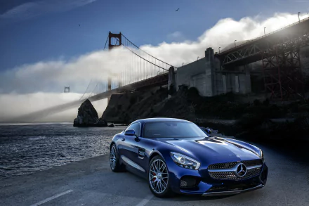 A stunning blue Mercedes-AMG GT parked by the water, with the iconic Golden Gate Bridge shrouded in fog in the background, captures the essence of luxury and performance.