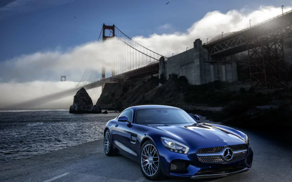A stunning blue Mercedes-AMG GT parked by the water, with the iconic Golden Gate Bridge shrouded in fog in the background, captures the essence of luxury and performance.