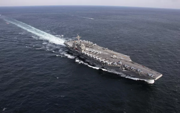 Aerial view of the USS Abraham Lincoln (CVN-72) aircraft carrier sailing in open sea, showcasing its military presence and deck operations.