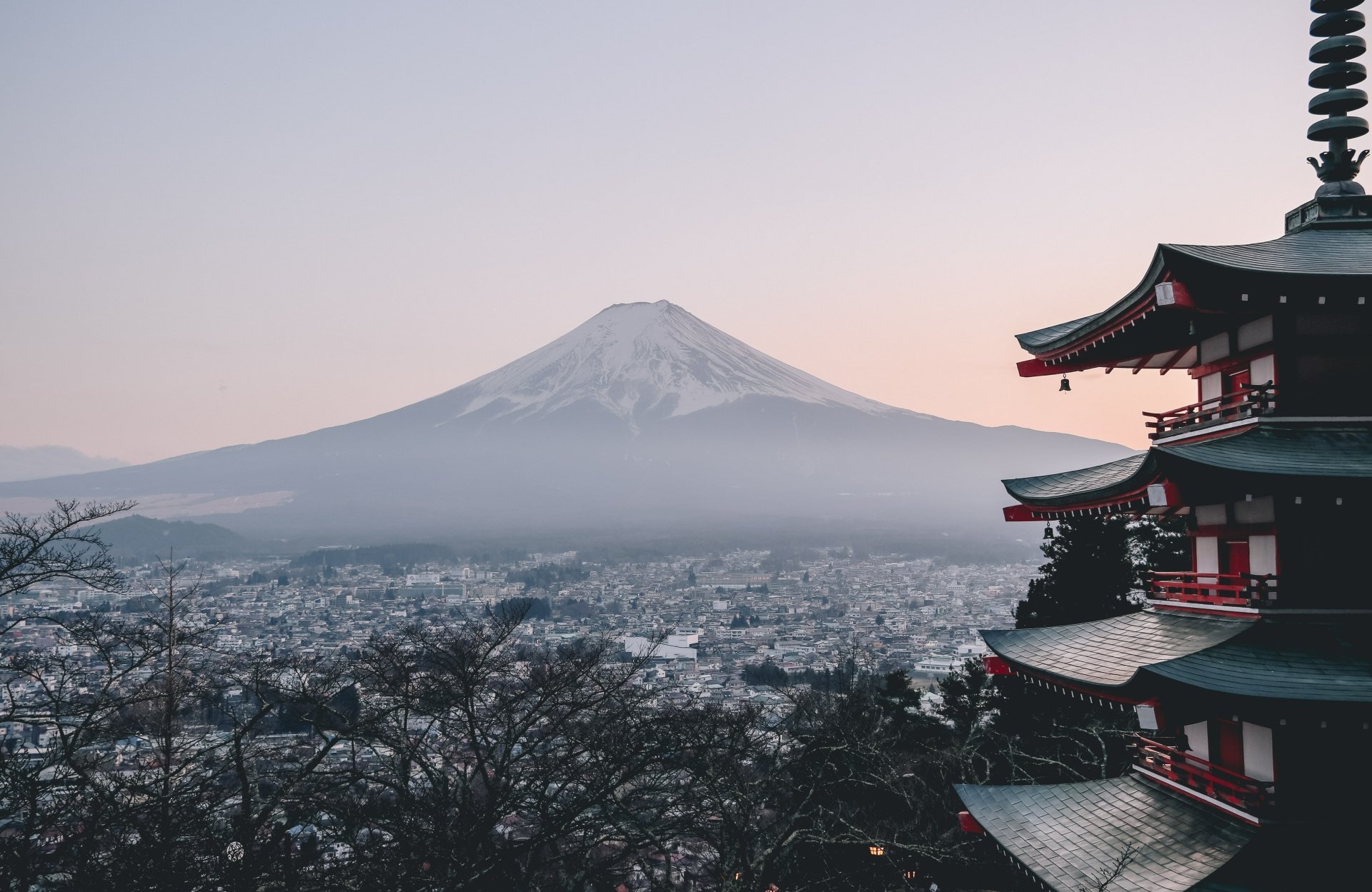 4K Ultra HD view of Mount Fuji rising above a peaceful town in Japan, framed by traditional pagoda architecture and tranquil natural surroundings at dusk.