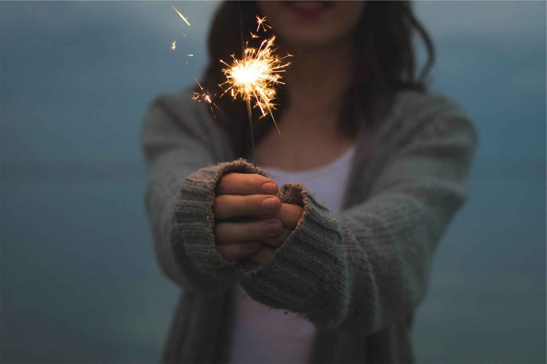 A person holding a lit sparkler glowing against a dim, blurred background, capturing light and fireworks in an HD PC desktop wallpaper style.