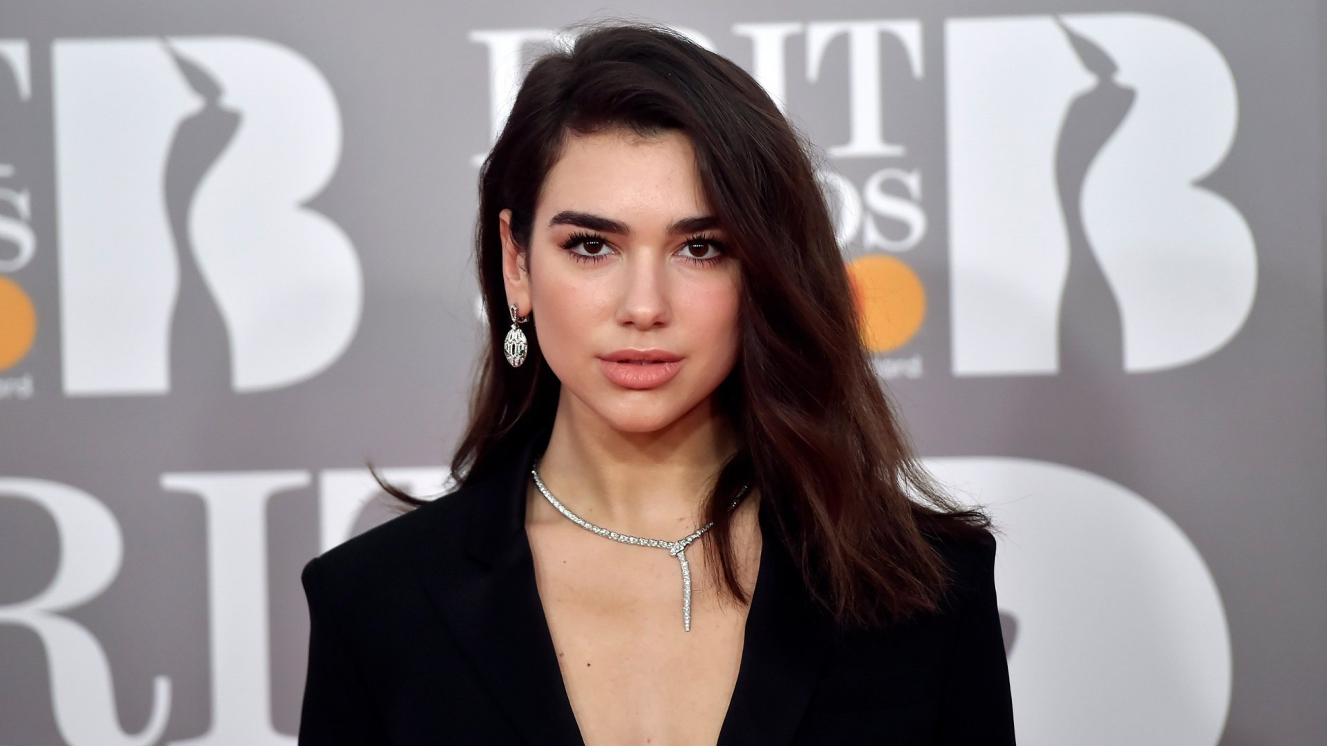 HD desktop wallpaper featuring English singer Dua Lipa with brunette hair and brown eyes, dressed elegantly at a music awards event.