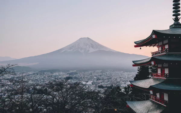 4K Ultra HD view of Mount Fuji rising above a peaceful town in Japan, framed by traditional pagoda architecture and tranquil natural surroundings at dusk.