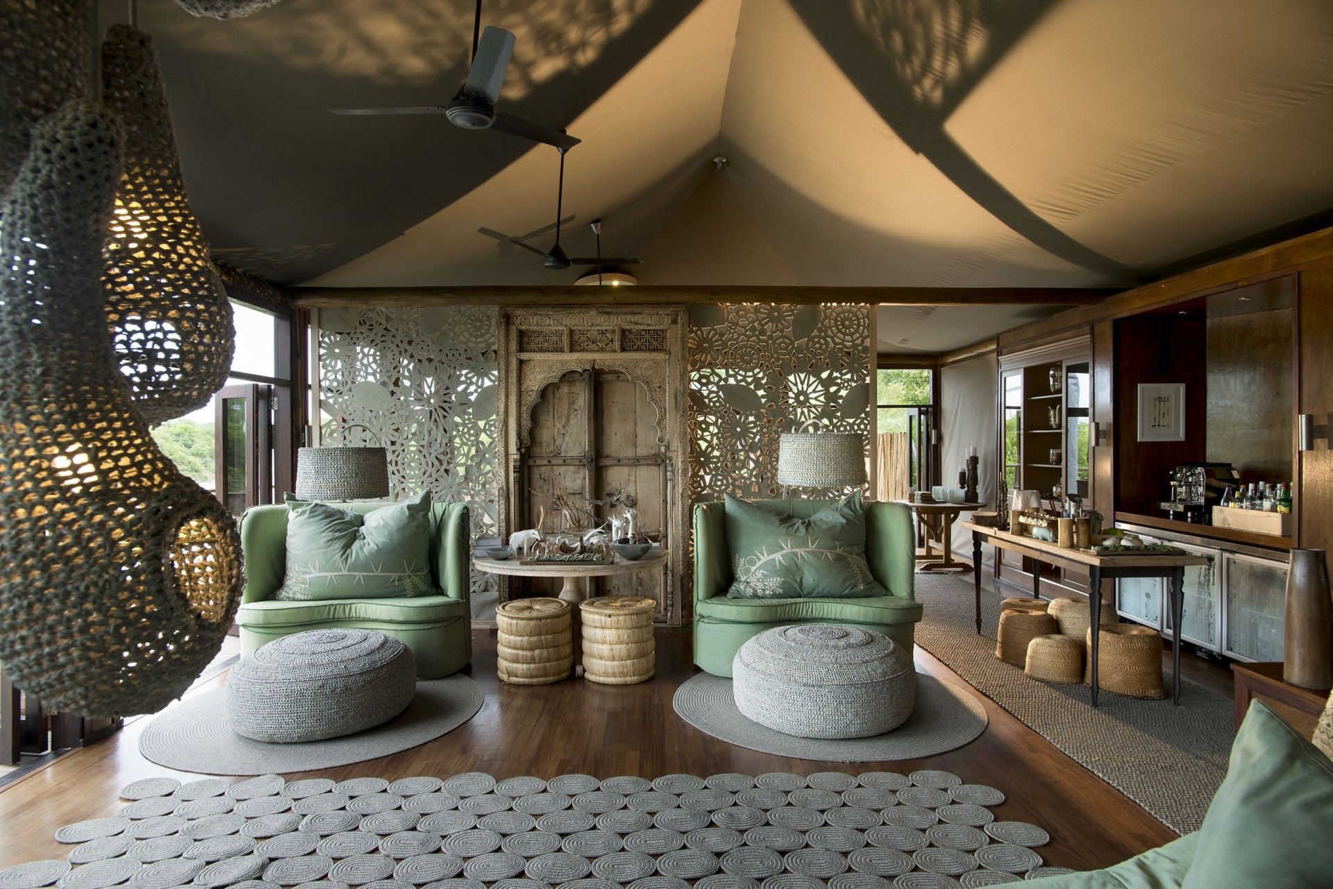 HD PC desktop wallpaper showcasing a modern living room with green armchairs, woven ottomans, textured room dividers, and ambient lighting in a stylish, man-made space.